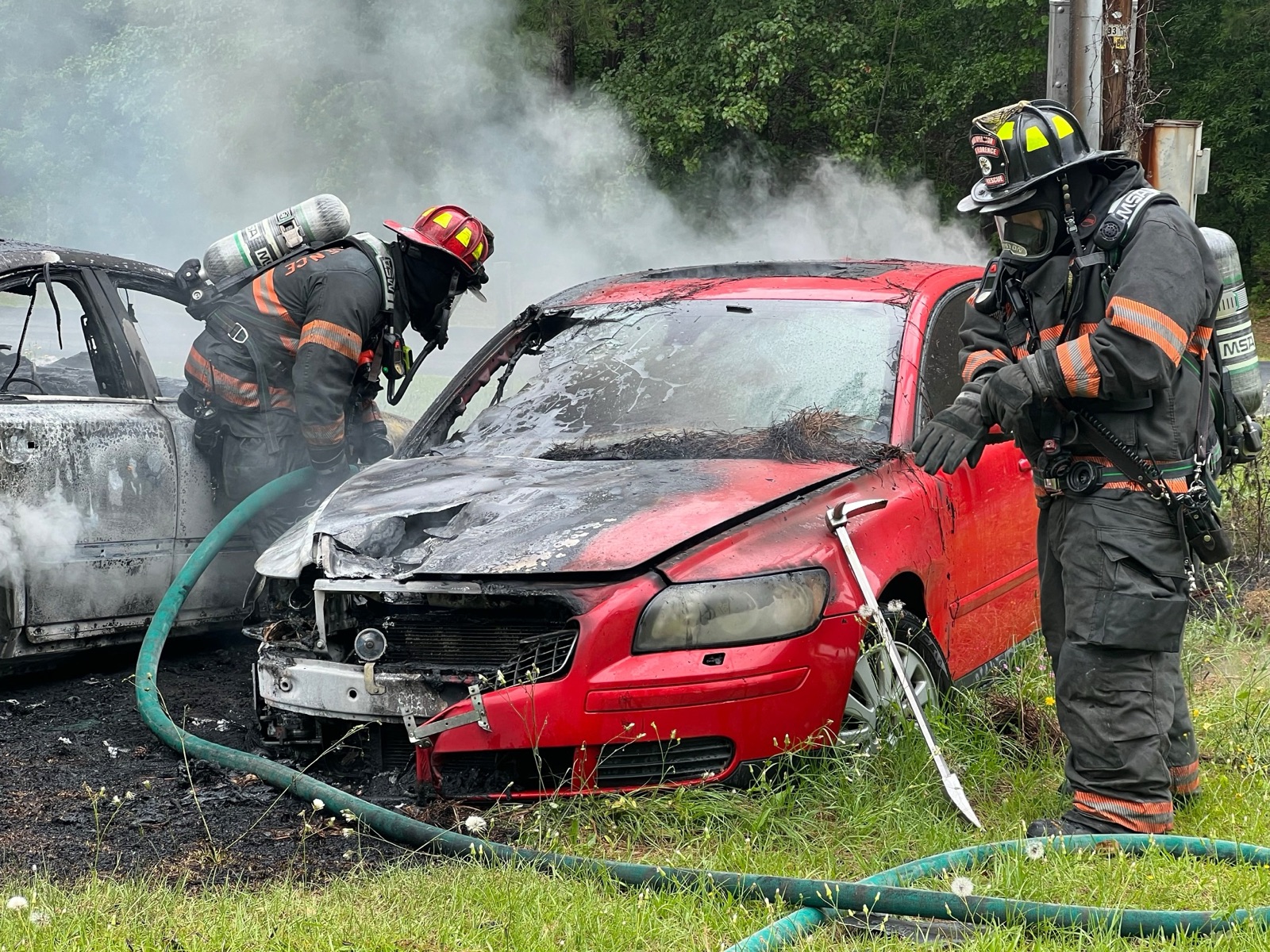 Two firefighters in full turnout gear overhauling a passenger vehicle after a fire