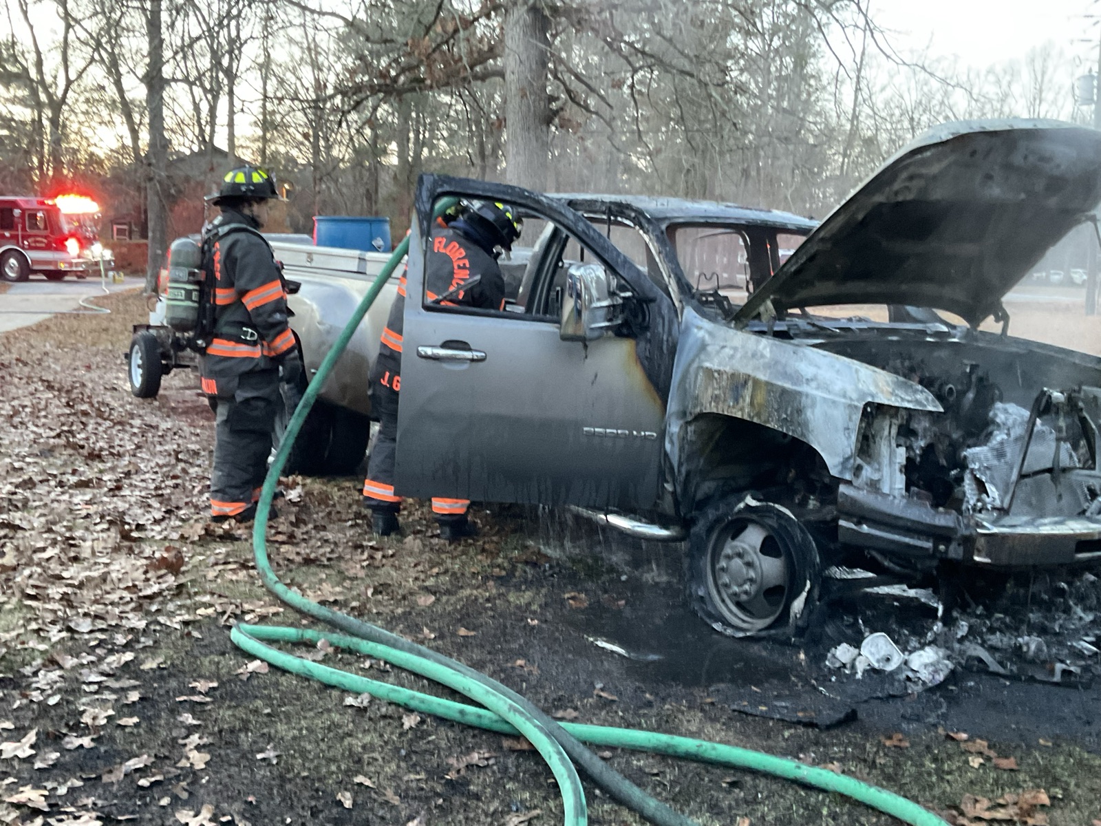 Two firefighters in turnout gear working a burned pickup truck at dawn