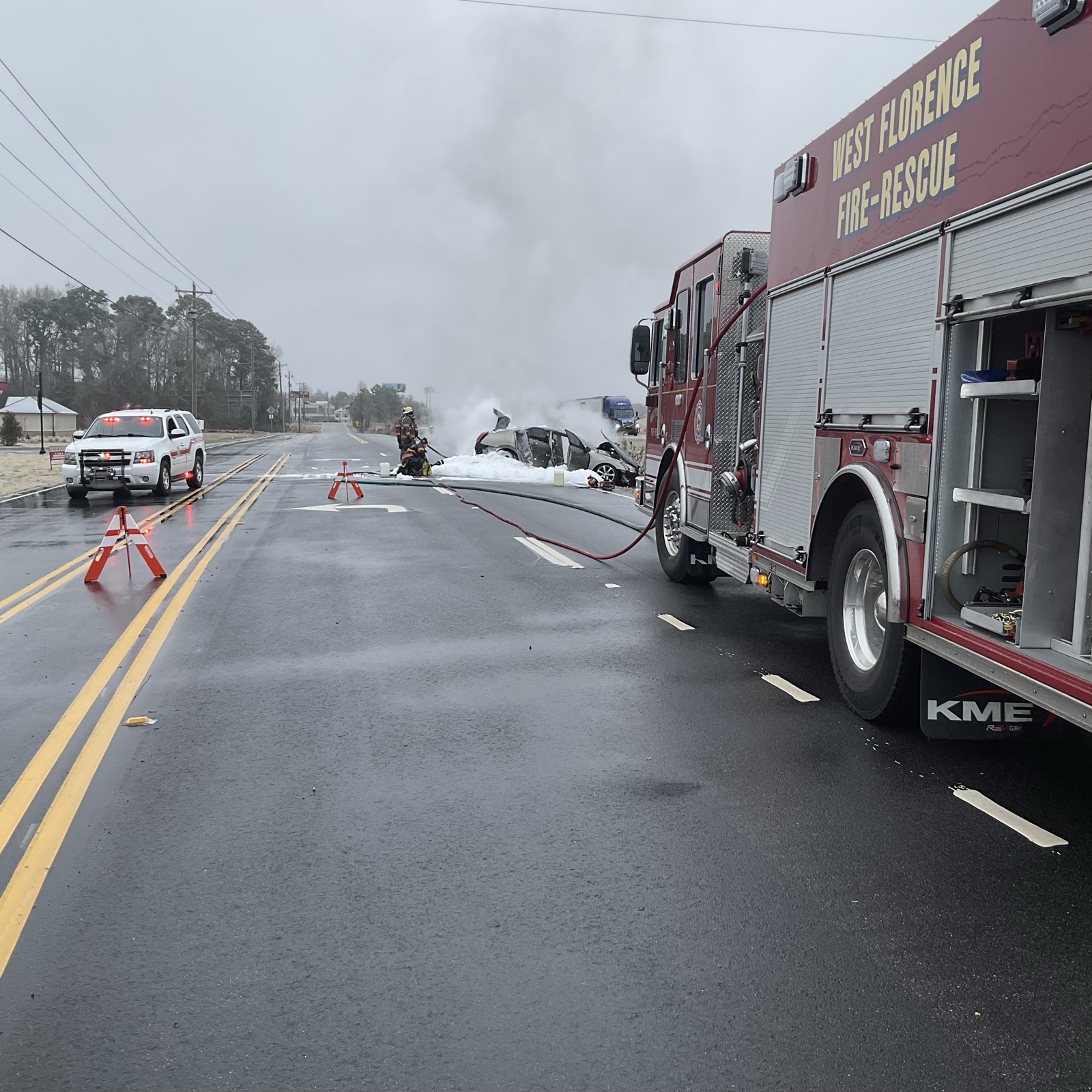 West Florence engine staged on a highway in winter weather, crew working a foamed-down vehicle in the distance