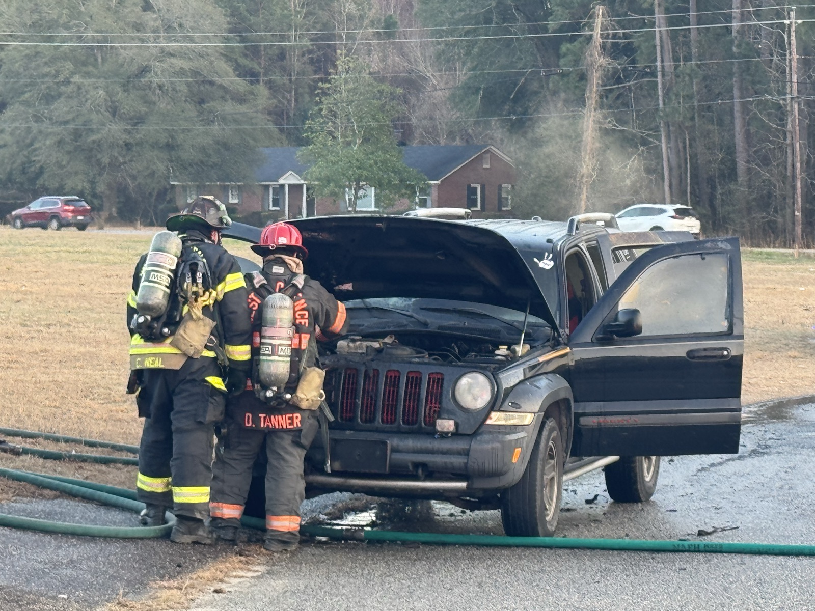 Two firefighters in full turnout gear overhauling a Jeep after a vehicle fire